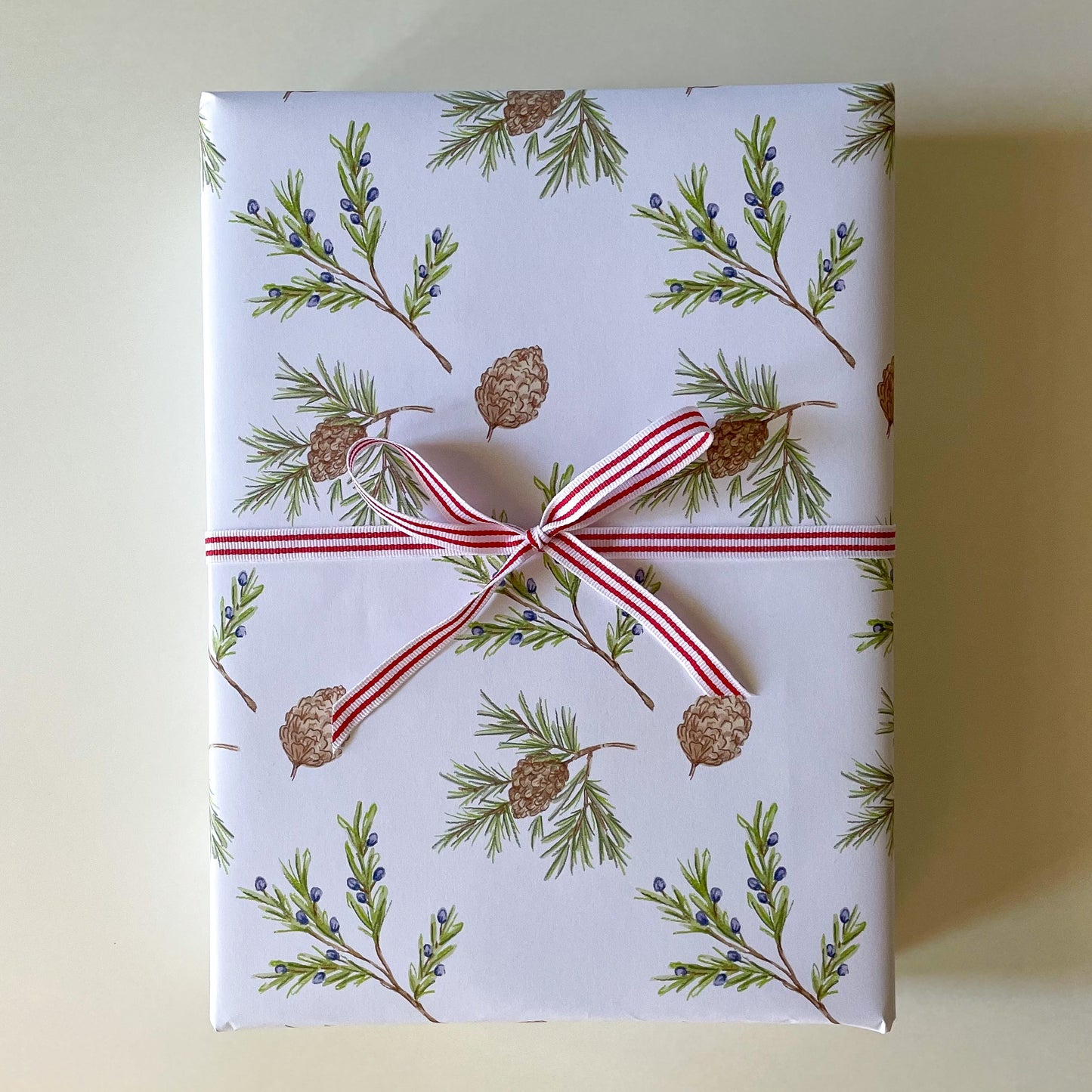 Gift box wrapped in paper with greenery design and red ribbon on a light background